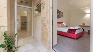 A bedroom with a red bed, a small kitchen in the background, and a stone wall. - Liberty Barocco - Matrimoniale Standard (Lecce)