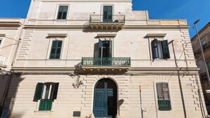 A building with a central entrance, a balcony with green railings, and multiple windows with shutters. - Liberty Barocco - Matrimoniale Standard (Lecce)