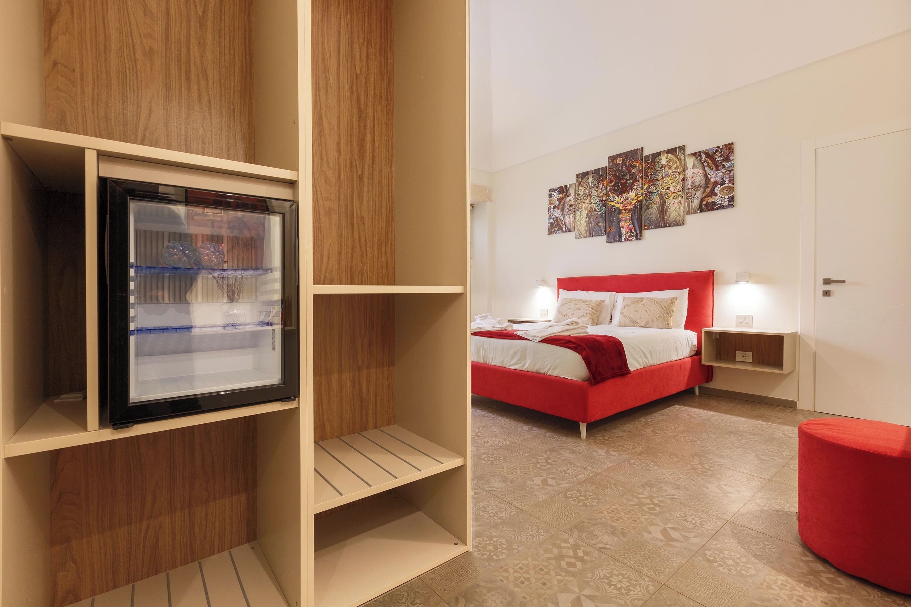 Une chambre avec un lit rouge, une armoire en bois et un pouf rouge.