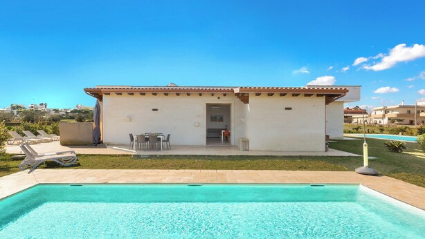 Ein modernes Haus mit Swimmingpool, einer Terrasse mit Liegestühlen und einem kleinen Essbereich.