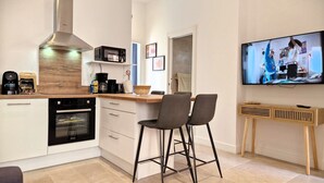 Een moderne keuken met een ingebouwde oven, magnetron en koffiezetapparaat. Er zijn twee barkrukken en een televisie aan de muur bevestigd.