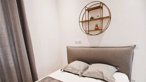 Een slaapkamer met een bed, een hoofdbord, een wandplank met decoratieve objecten en een gordijn.