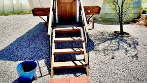 A covered structure with a wooden door labeled "JONES," a set of wooden steps leading up to it, and a small tree nearby.