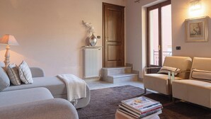 Een woonkamer met een bank, fauteuils, een lamp, een radiator en een deur naar een balkon.