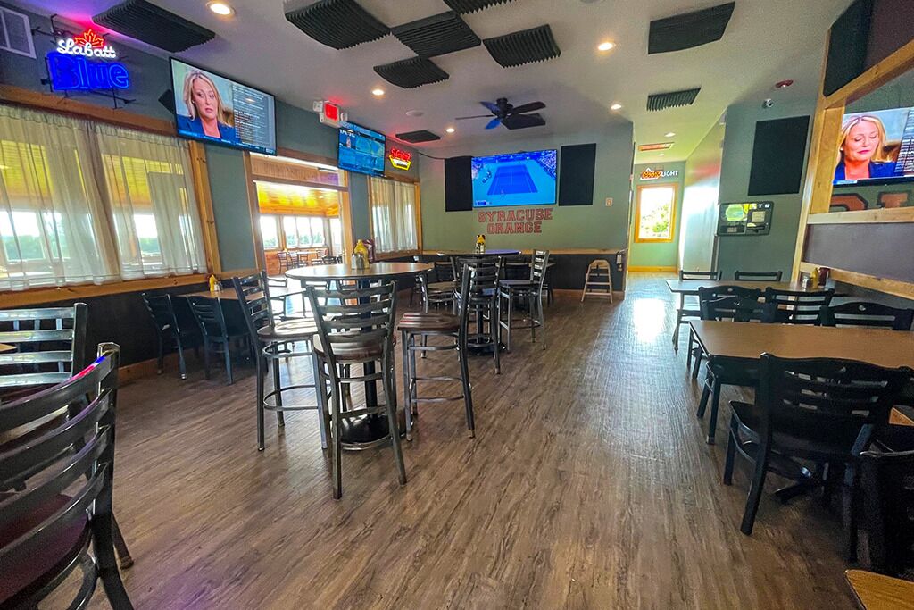 A restaurant interior with multiple tables and chairs, a television screen, and a ceiling fan.