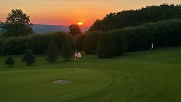 A golf course at sunset with a flag, trees, and a clear sky.