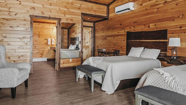 Une pièce de cabane en bois comprenant deux lits, un banc, une chaise, une table et un miroir.