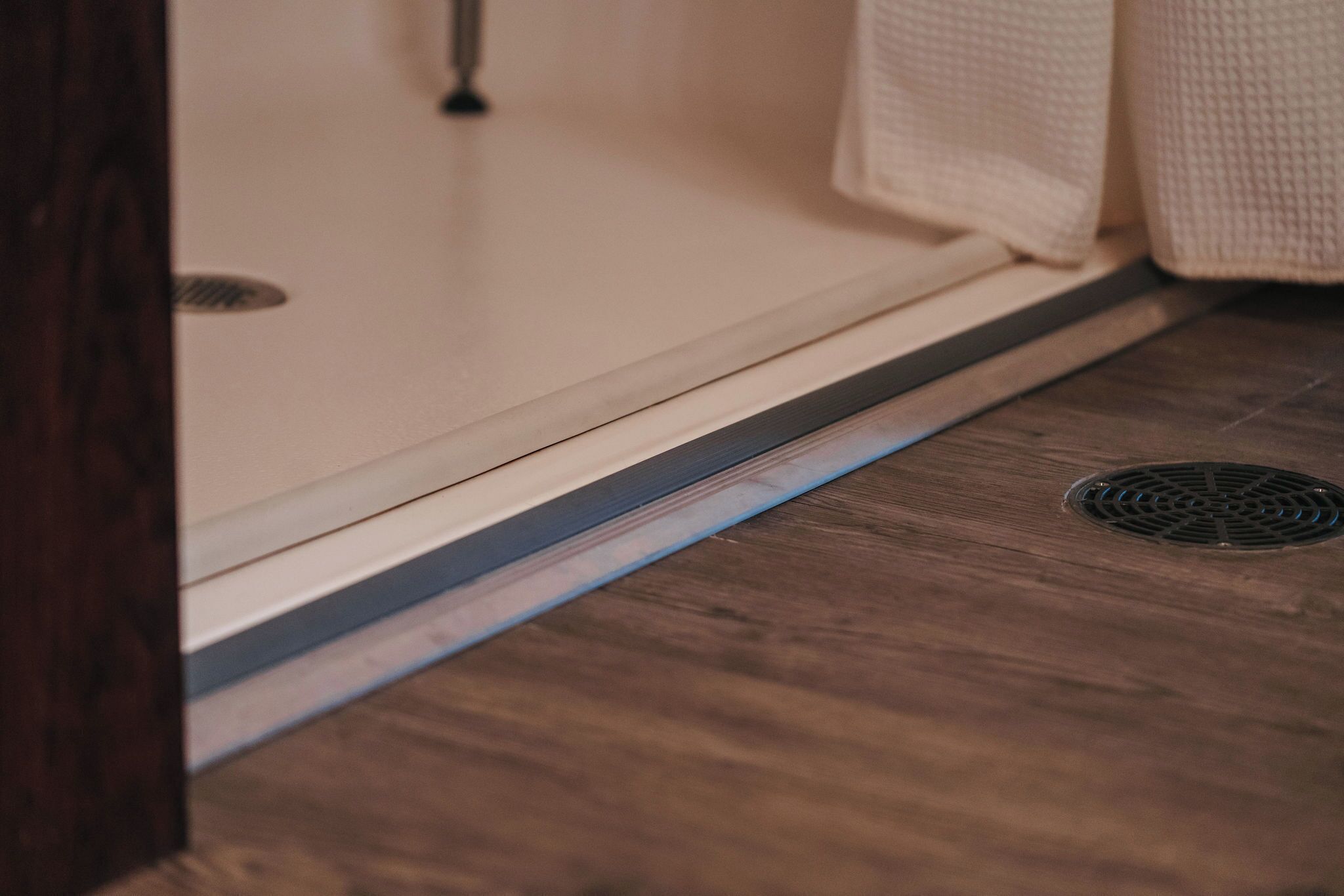 A wooden floor with a vent and a white shower door.
