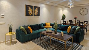 A modern living room with a green sofa, a wooden coffee table, and a dining area with a wooden table and chairs.