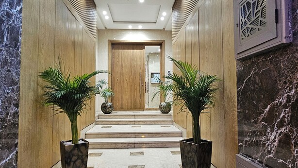 A modern hallway with marble flooring, wooden paneling, and two potted plants.