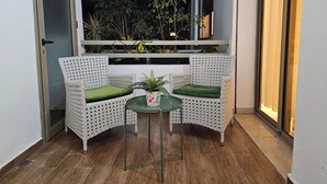 A small outdoor seating area with two wicker chairs and a table, surrounded by potted plants and a view of the night sky.
