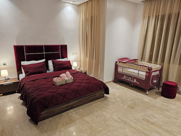 Habitación de hotel con una cama grande, una mesita de noche con lámpara y una cuna con cambiador.