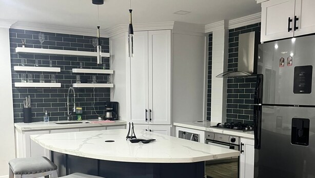 Una cocina moderna con una isla central, armarios blancos y electrodomésticos de acero inoxidable.
