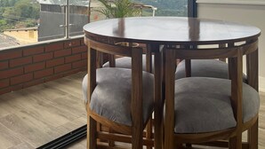Un balcón con una mesa y sillas de madera redondas, vista del paisaje y una ventana con persianas.