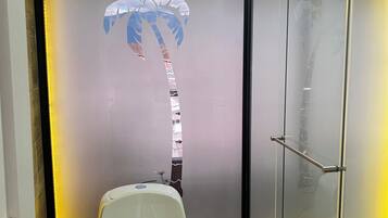 A bathroom with a toilet, a glass shower enclosure, and a frosted glass wall with a palm tree design.