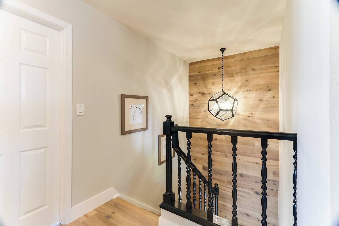 A staircase with a wooden finish and a black balustrade, leading to a room with a white door and a wooden wall.