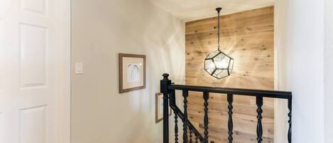 A staircase with a wooden finish and a black balustrade, leading to a room with a white door and a wooden wall.