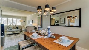 Un comedor con una mesa de madera dispuesta para cuatro personas, una lámpara de araña y un espejo grande sobre la mesa.