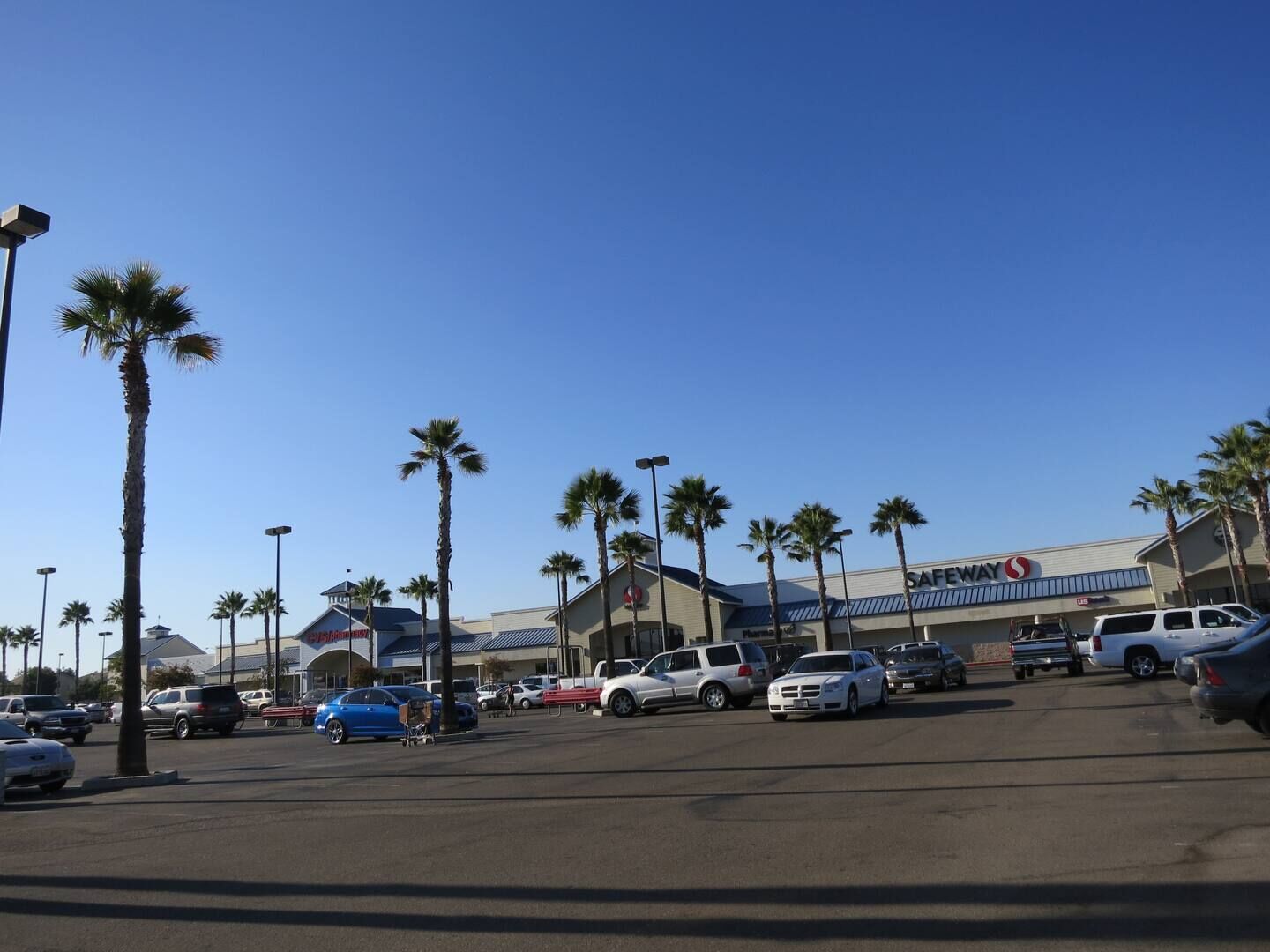 Un negozio Safeway con un parcheggio, palme e diverse automobili.