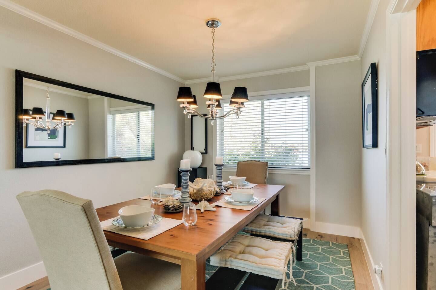 Un comedor con una mesa de madera, sillas, una araña y un espejo grande.