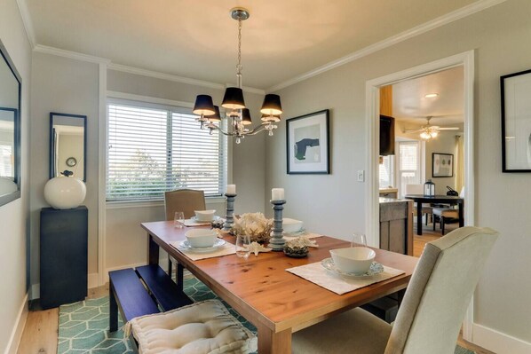 A dining area with a wooden table, benches, and a chandelier. There are framed pictures on the walls and a window with blinds. - CHARMING 3 BEDROOM LAKE FRONT HOUSE WITH FAST WIFI IN DISCOVERY BAY (Discovery Bay)
