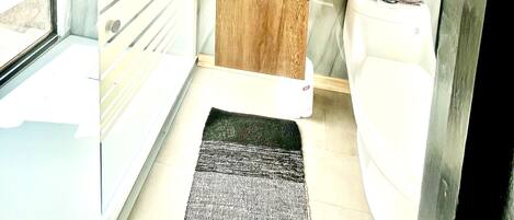 Un baño moderno con cabina de ducha de vidrio, tocador de madera, inodoro blanco y espejo con marco negro.