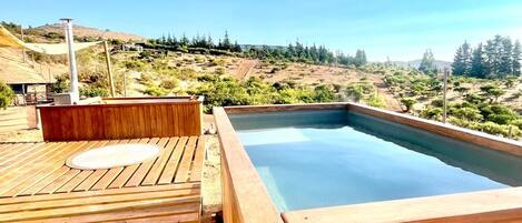 A wooden deck with a hot tub and a view of a hilly landscape.