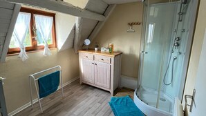 A small, cozy room with a sloped ceiling, a wooden cabinet, a small table, a shower area, and a window with curtains. - Charming gîte, former wine estate, sleeps 13 (Orschwihr)