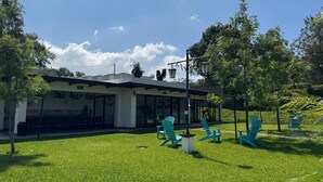 Ein Gebäude mit modernem Design, großen Fenstern und einem überdachten Außenbereich mit grünen Stühlen und Tischen.