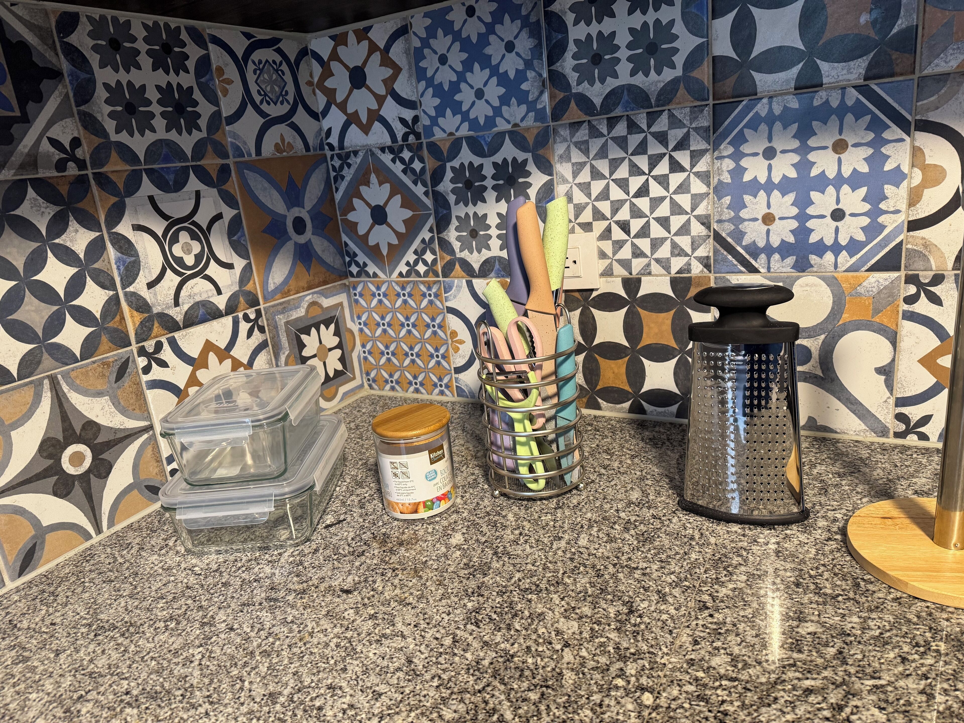 Una encimera de cocina con diversos utensilios y recipientes, incluyendo un rallador y un tarro de especias.