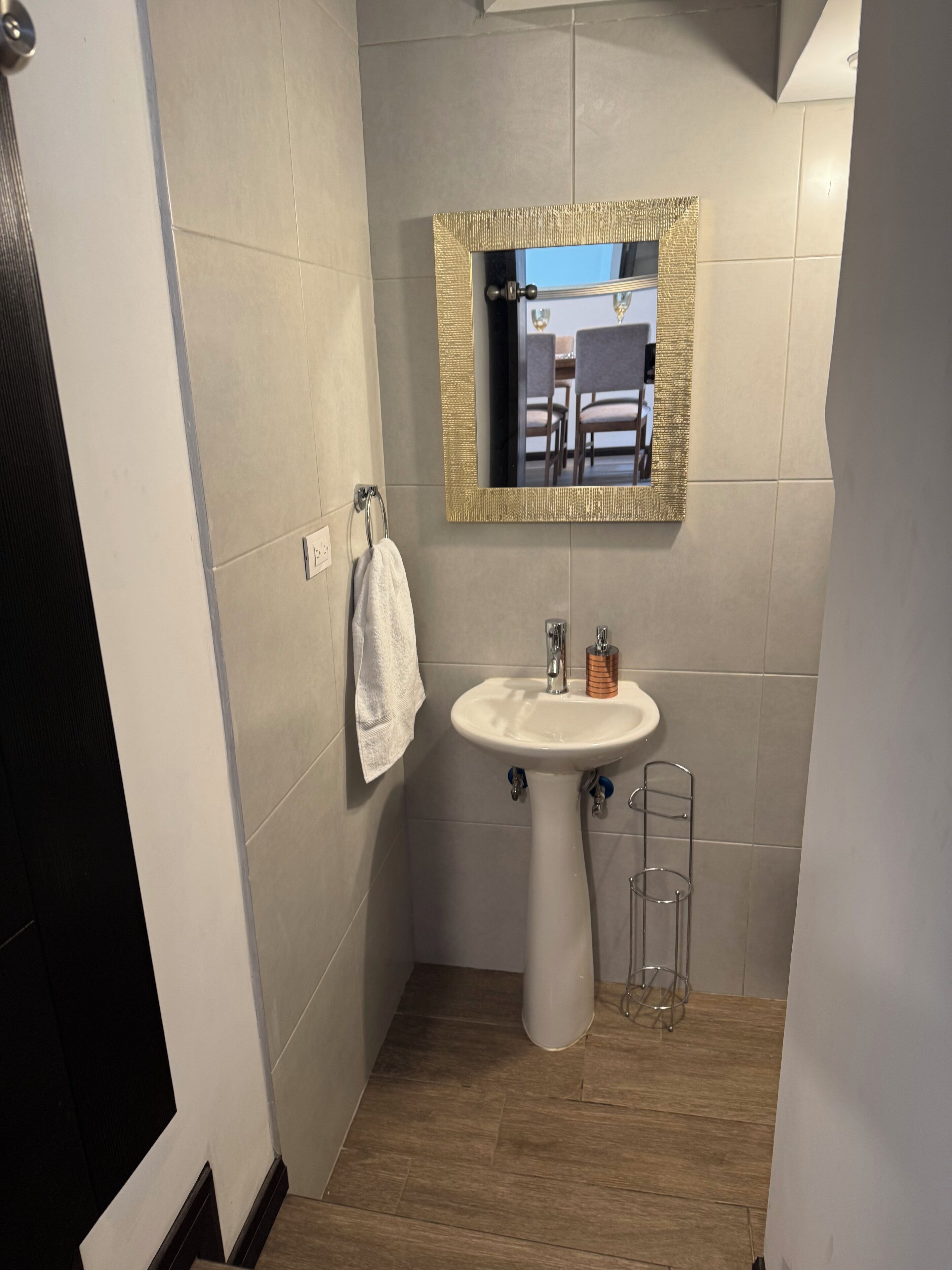 Een badkamer met een witte wastafel, een spiegel met gouden lijst en een handdoek aan een rek.