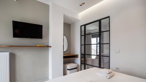 Ein modernes Hotelzimmer mit einem Bett, einem flachbildfernseher an der Wand, einem großen Spiegel und einer Glastür, die auf einen Balkon führt.