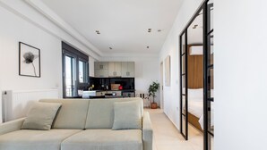 Ein modernes Wohnzimmer mit einer Couch, einer Küche im Hintergrund und einer Schiebetür, die zum Schlafzimmer führt.