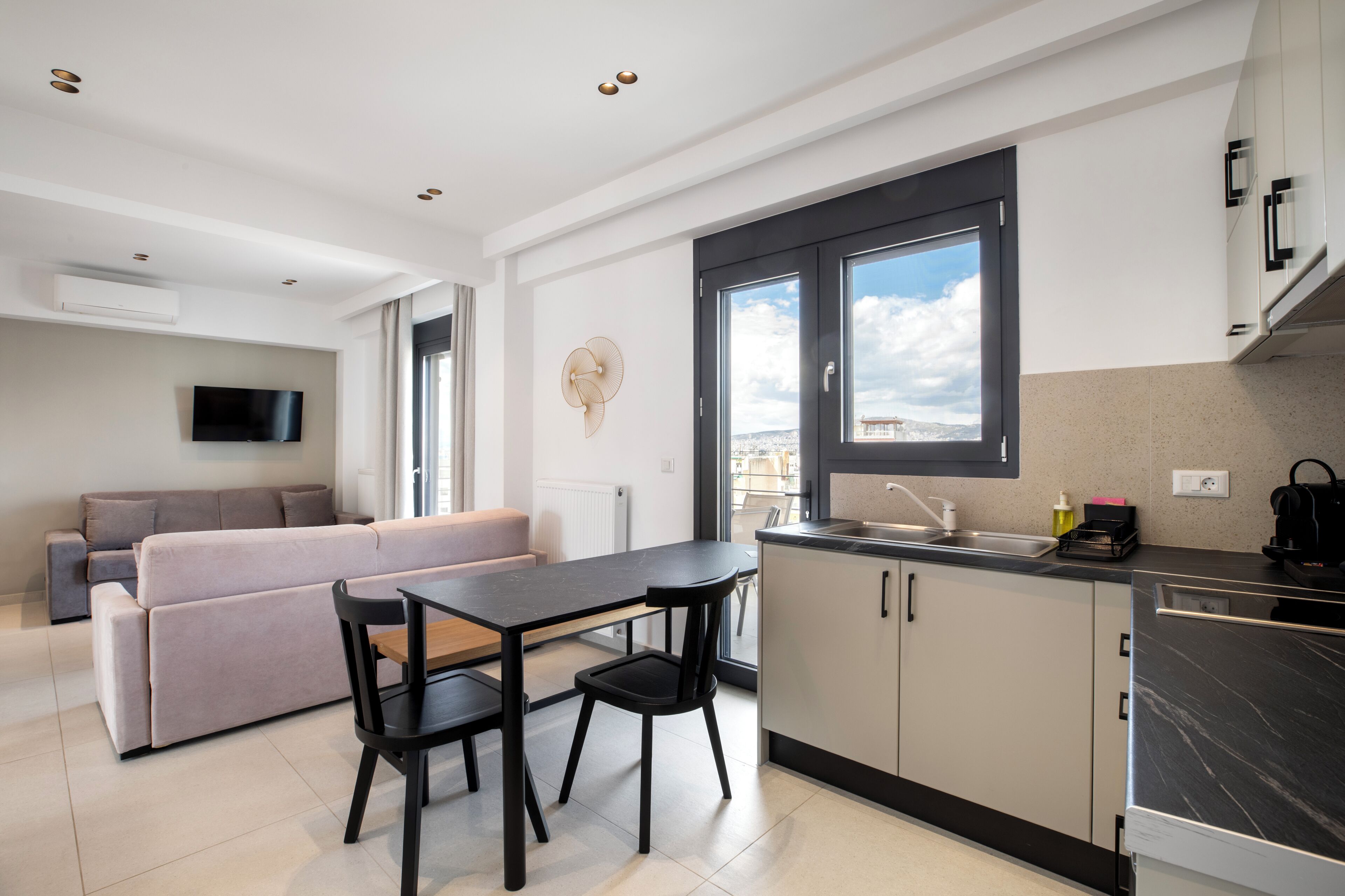 A modern kitchen with a dining area, a sofa, and a TV in a bright living space.