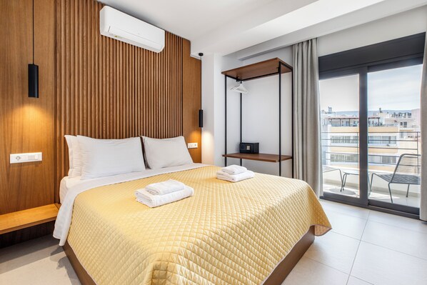 A hotel room with a bed, a wooden panel wall, an air conditioning unit, a desk, and a balcony with a view. - Athens Genesis Luxury Suites (Athens)