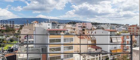 A balcony with a table and chairs, overlooking a cityscape with buildings and a distant mountain.
