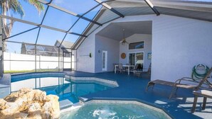 A swimming pool with a glass enclosure, a hot tub, and a patio area with chairs and a table.