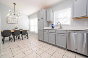 A modern kitchen with grey cabinets, a stainless steel dishwasher, and a dining area with a table and chairs.