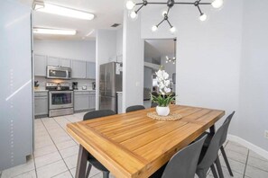 A modern kitchen with stainless steel appliances, a wooden dining table with chairs, and a hanging light fixture.