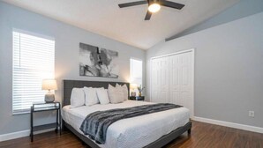 A bedroom with a bed, a ceiling fan, a nightstand, a lamp, and a door.