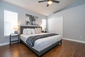 A bedroom with a bed, a ceiling fan, a nightstand, a lamp, and a door. - 4 Miles to Disney! Private pool -5 Bedroom Home (Kissimmee)