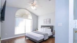 A bedroom with a bed, a ceiling fan, a TV mounted on the wall, and a window with blinds. - 4 Miles to Disney! Private pool -5 Bedroom Home (Kissimmee)