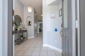 A hallway with a tiled floor, a console table with a mirror, a potted plant, and a blue vase on a counter.