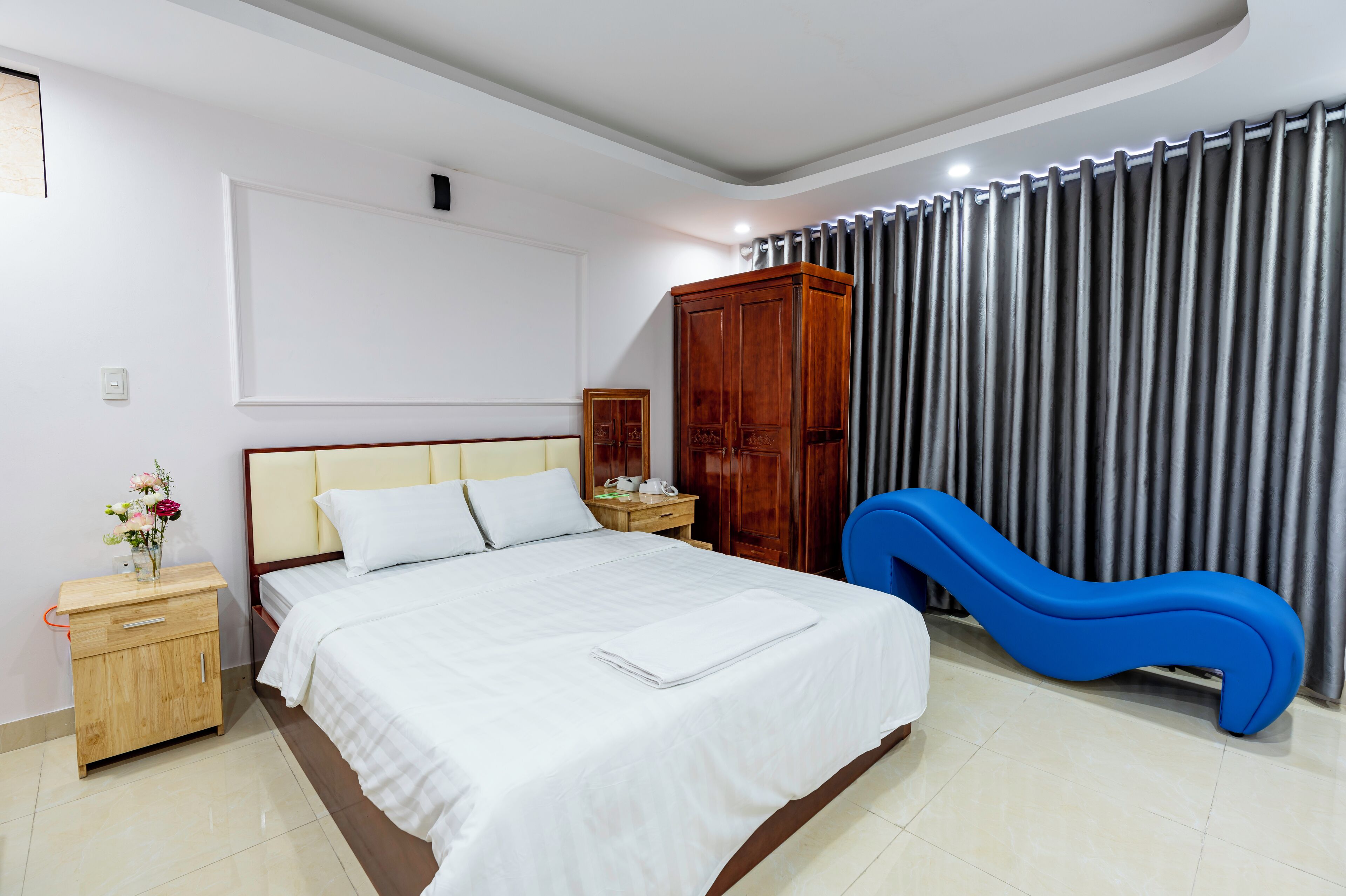 A hotel room with a bed, a nightstand, a wardrobe, and a blue chair.