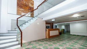 Un hall d’entrée spacieux avec un mur de marbre, un escalier doté de rampes en verre et un sol recouvert de carreaux décoratifs.