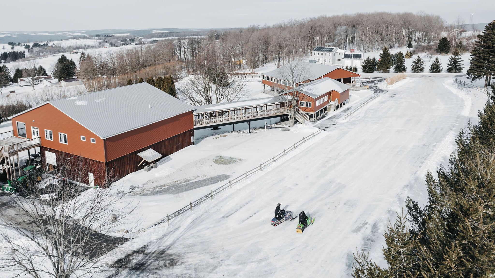 A snow-covered landscape with a ski lift, a red barn, and a snowmobile track.