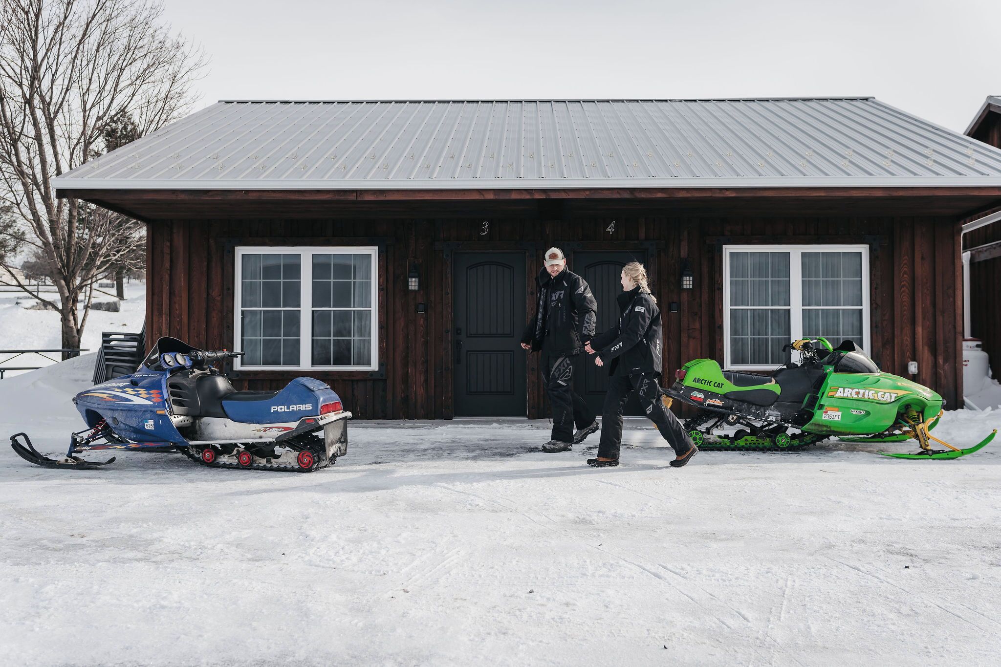 A wooden building with two snowmobiles parked in front.