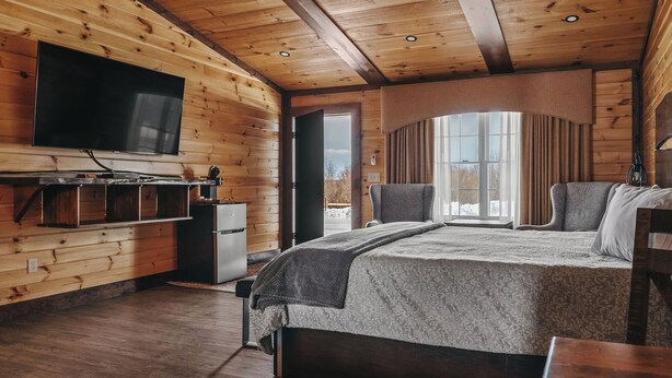 A log cabin bedroom with a large bed, a TV mounted on the wall, and a window with curtains. - Golf, Outdoor Bar, Restaurant - The Forest Haven (Tully)