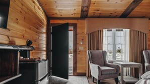 A cozy cabin interior with wooden walls, a fireplace, a dining area with a table and chairs, and a window with curtains. - Golf, Outdoor Bar, Restaurant - The Forest Haven (Tully)