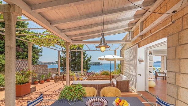 An outdoor patio with a table set for dining, surrounded by wicker furniture and potted plants.